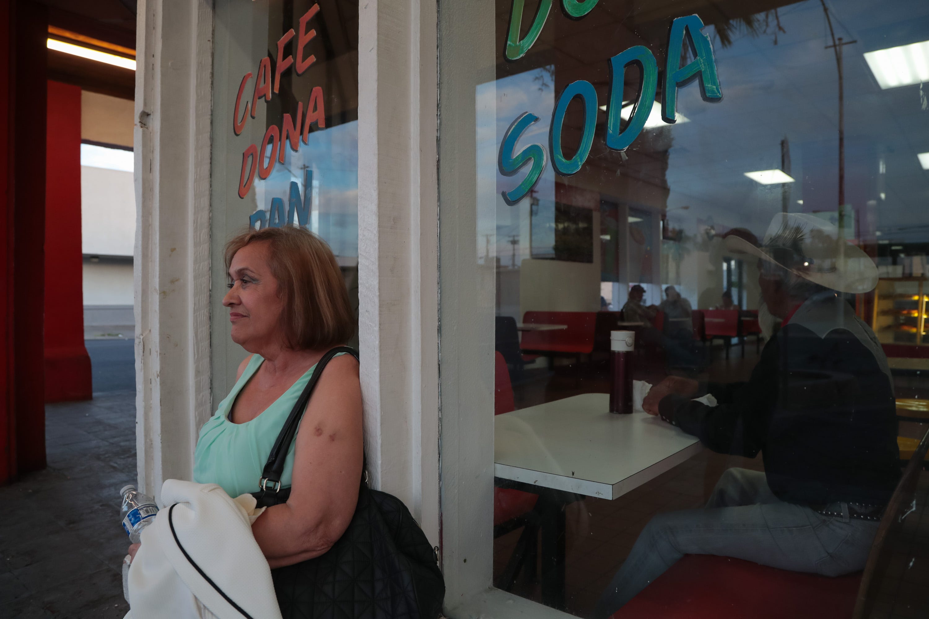 Gloria Barraza sits outside of Donut Avenue after waiting all night for a bus to Brawley, Calexico, Calif., 5:44 AM, June 12, 2019.  A man she identified as her boyfriend sits at the table behind her inside.