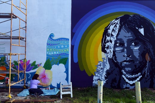 Local artist Carol Makris continues work on a new mural on Thursday, June 20, 2019 on the back wall of the Firestone Complete Auto Care building in downtown Vero Beach. The new mural, which is going up next to a mural of a Seminole Indian by Brooke Malone, will feature images of plants and wildlife native to Florida. Makris' mural is part of the Downtown Vero Beach Mural Project.