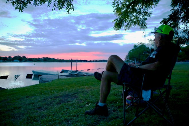Charlie Lovelace watches the sun rise as he waits for the drag boat races to start at Lake Nasworthy on Saturday, June 22, 2019.