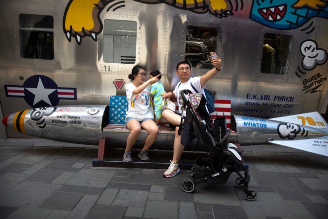 A family poses for a selfie while sitting on a bench shaped like a missile painted with the U.S. flag outside of a clothing store at a shopping mall in Beijing, Saturday, June 29, 2019.