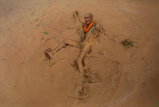An elderly Nepalese man falls in the mud in a paddy field while playing with another during Asar Pandra, or paddy plantation day in Dhading district, Nepal. Nepalese Hindus consider Asar Pandra an auspicious day for planting paddy. 