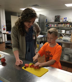 Anna Westmark, community health educator with the Kewaunee County Public Health Department, helps a student slice tomatoes during a nutrition and cooking class offered by the department in June at Algoma Middle School.