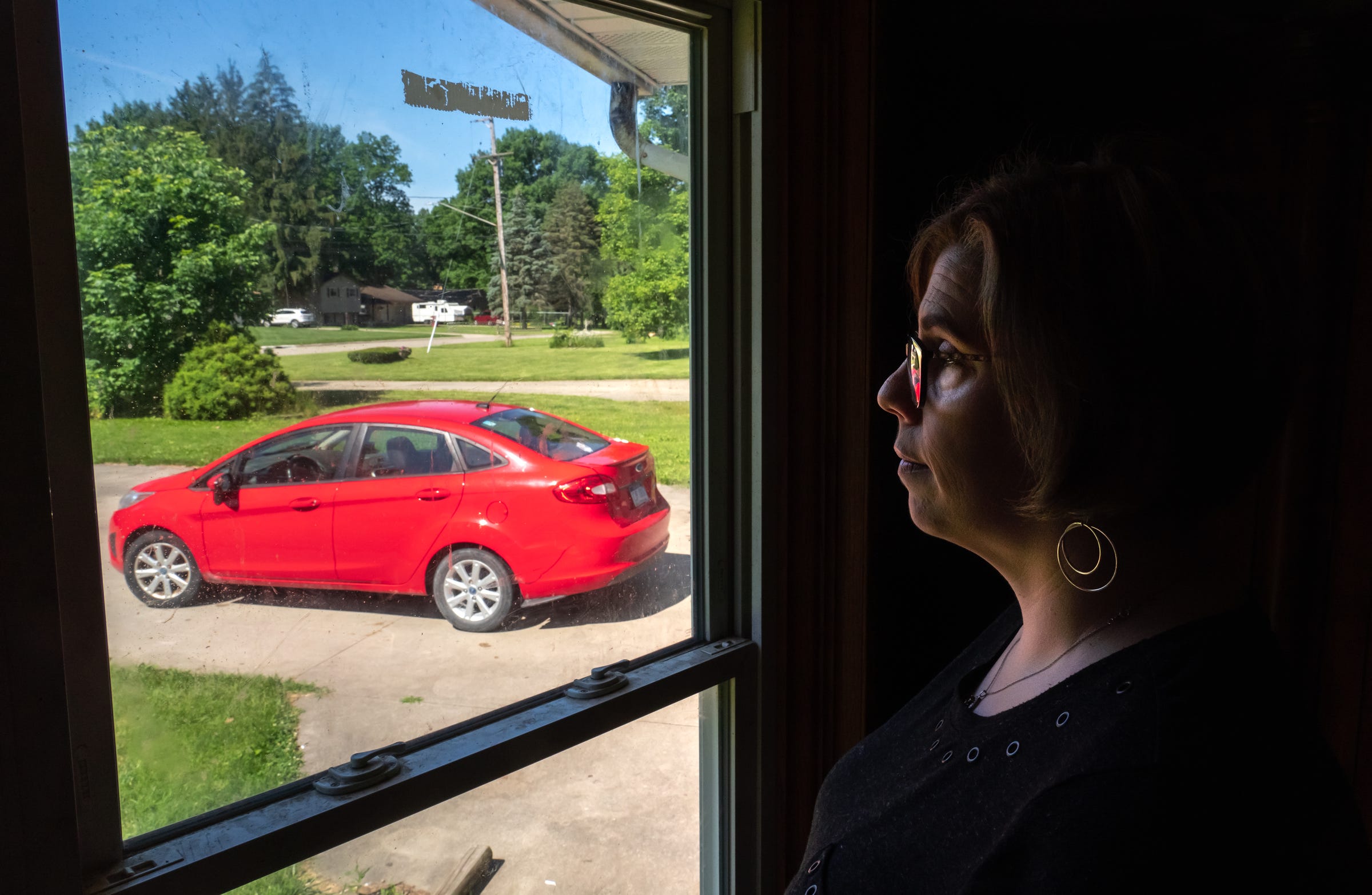 Michelle Hughes looks out the window toward her 2012 Ford Fiesta parked at her home in Flint on Wednesday, June 26, 2019. "It got me to and from work for quite a few years and now it just sits in the driveway," Hughes said, about her car plagued with a transmission problem that only drives when necessary due to safety concerns. "I trusted Ford and I shouldn't have."