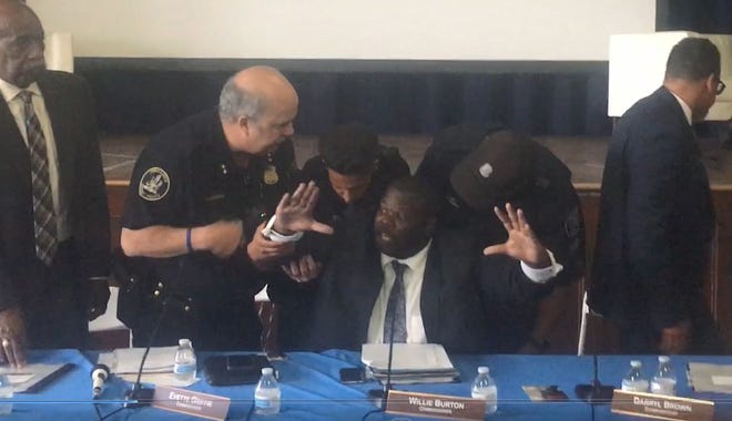 Police officers remove police commissioner Willie Burton from a board meeting where facial recognition software was discussed