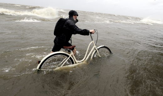 Tyler Holland guides his bike through the water as winds from Tropical Storm Barry push water from Lake Pontchartrain over the seawall, July 13, 2019, in Mandeville, La.