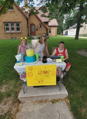 Addison (left), Kaylen (middle) and Aidan (right), are ready for customers at their lemonade stand. A replica of Zoey the police dog sits center above the homemade sign.