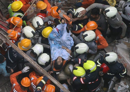 Rescuers carry out a survivor from the site of a building that collapsed in Mumbai, India on July 16, 2019. A four-story residential building collapsed Tuesday in a crowded neighborhood in Mumbai, India's financial and entertainment capital, and several people were feared trapped in the rubble, an official said.
