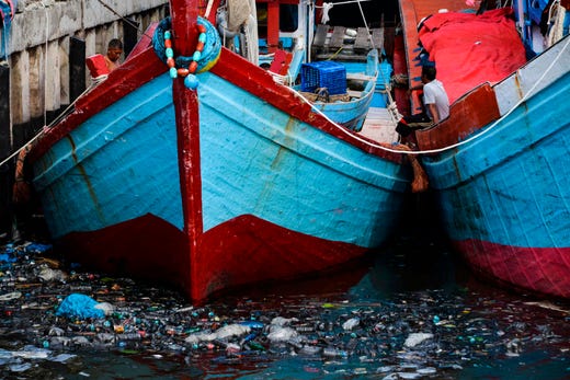Fishermen chat as garbage fills the waters around their boats at a fishing port in Banda Aceh on July 16, 2019.