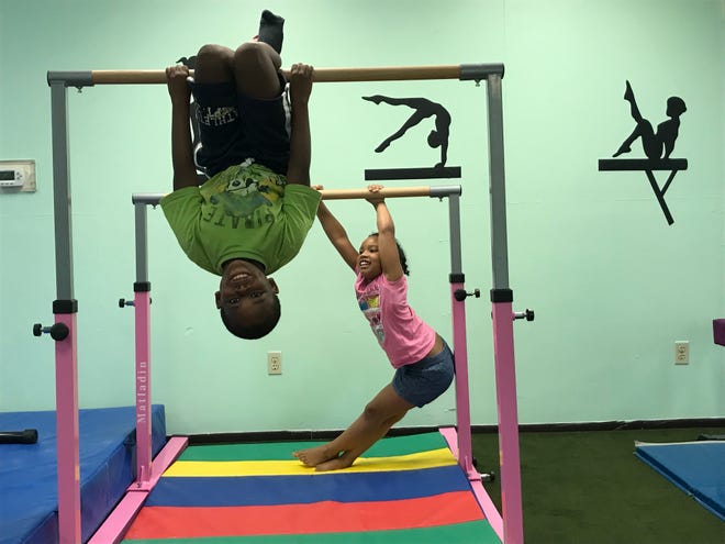 Naeem Paige, 9, hangs from the uneven bars while Victoria Perez, 7, holds on behind him. The two attend summer camp and participate in gymnastics at DARE Academy and DARE 2 Flip.
