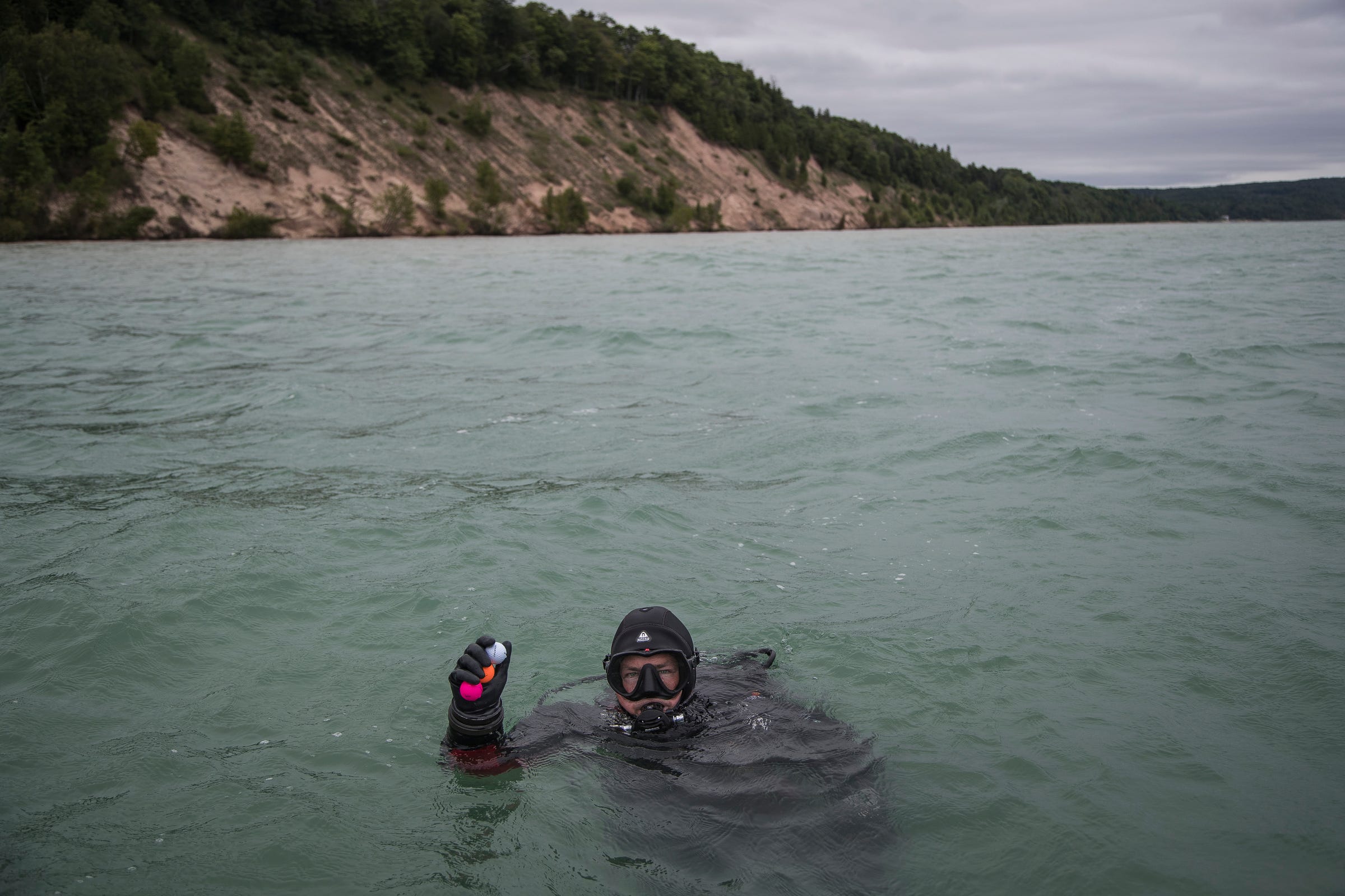 Diver Chris Roxburgh of Traverse City picks up some golf balls from Lake Michigan where ball have been teed from Arcadia Bluffs Golf Club's 12th tee box near Arcadia Township, Thursday, July 11, 2019.