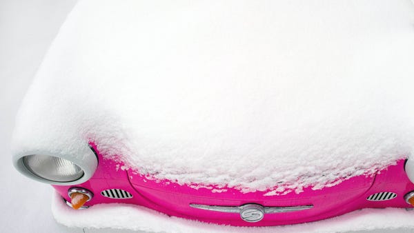 A pink Trabant car is covered in snow on a...