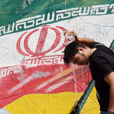 An Iranian cools off in front of a wall painting...