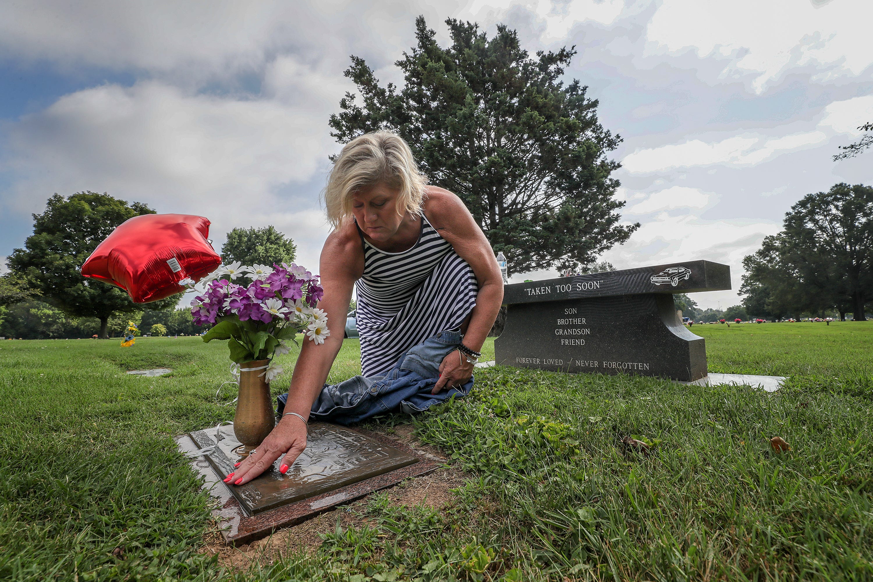 Michele Crockett, mother of Max Gilpin, uses some water and a shirt to wipe off her son's grave on what would have been Gilpin's 26th birthday. He died after becoming overheated at football practice at Pleasure Ridge Park High School. July 19, 2019