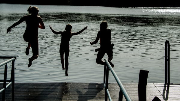 Children jump into the water from a dock at...
