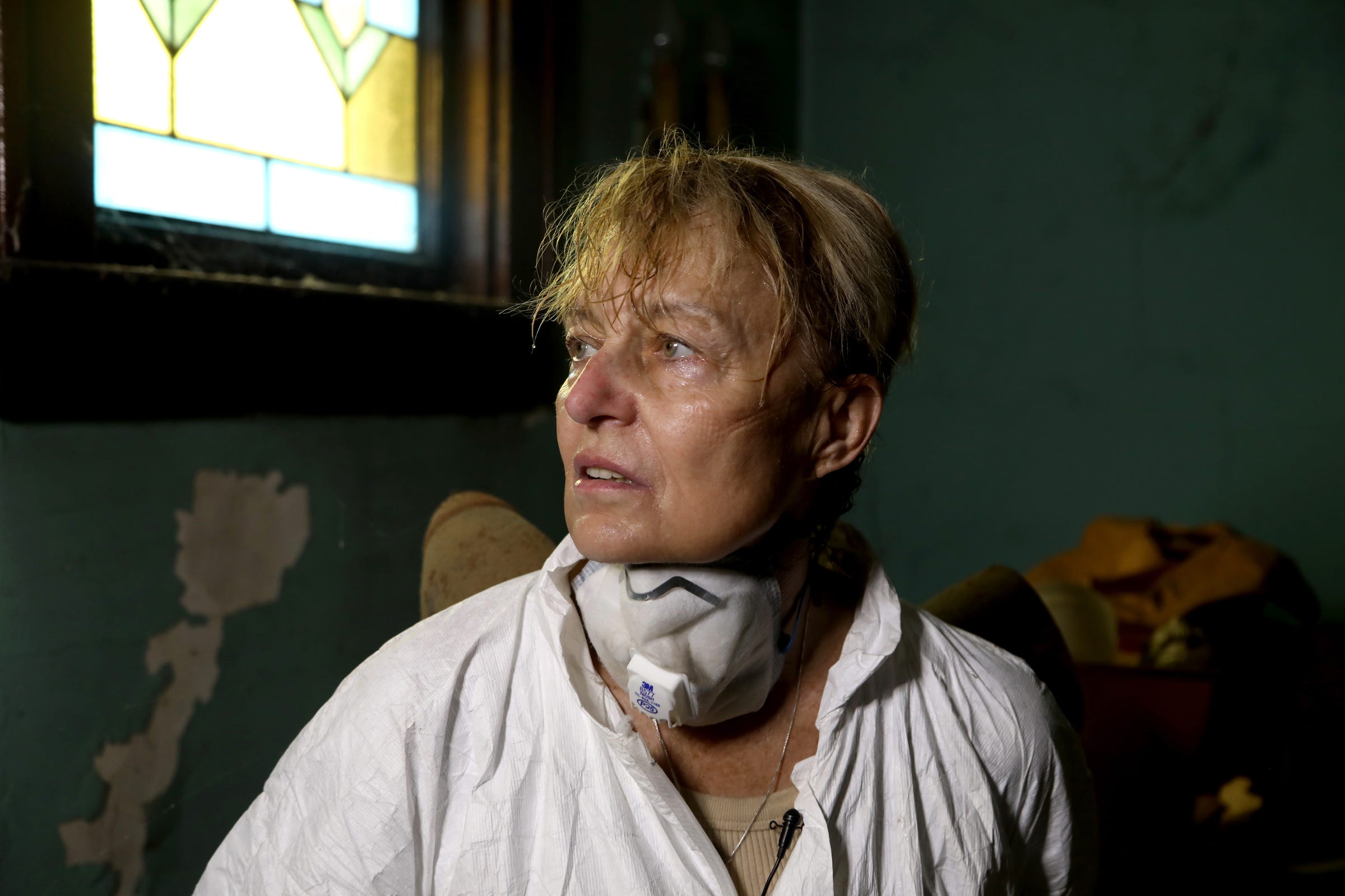 A sweaty Linda Kajma takes a break from cleaning out the front room of the house in Detroit that belonged to Sally and Lorraine Honeycheck, cousins of her mother on Saturday, July 6, 2019. Because of the smell from rat urine and droppings, untold amounts of mold and other items in the house Kajma has to wear non-breathable hazmat suit and mask for her safety.