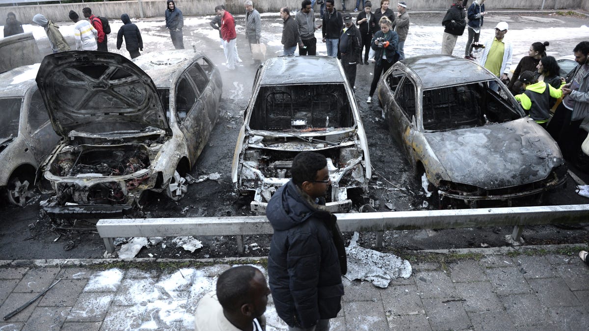 People inspect the scene where cars stand gutted by fire in the Stockholm suburb of Rinkeby after youths rioted in several different suburbs around Stockholm, on May 23, 2013.