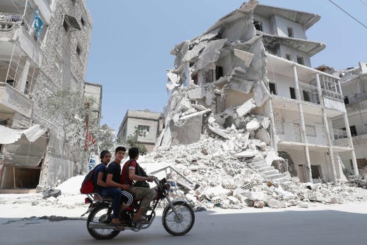 A Syrian man drives a motorcycle past destroyed buildings in the town of Ariha, in the south of Syria's Idlib province, on August 2, 2019.