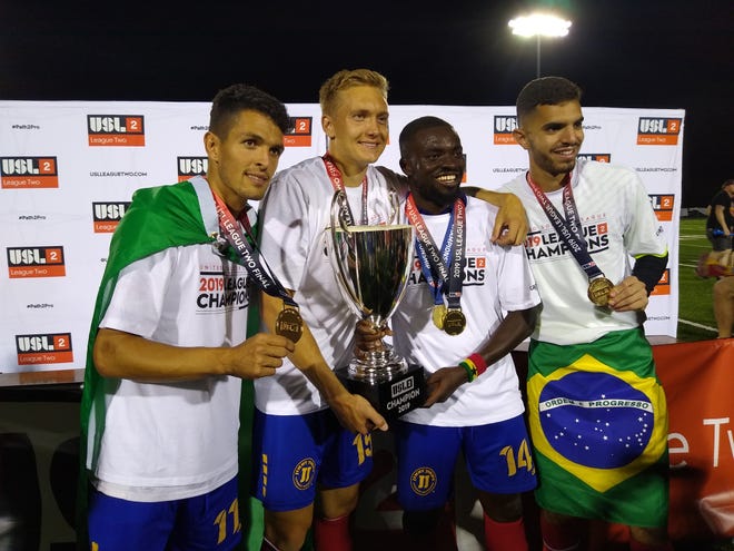 Flint City Bucks players Yuri Farkas Gugliemi, left; Charlie Booth, Foster Appiah and Gustavo Vasconcelos share a moment with the USL League 2 trophy after a 1-0 extra-time victory over Reading United AC before 7,198 fans at Atwood Stadium in August 2019.