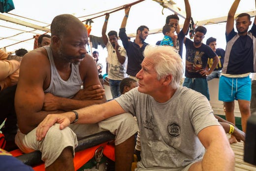 Actor Richard Gere, right, talks with migrants aboard the Open Arms Spanish humanitarian boat as it cruises in the Mediterranean Sea on Aug. 9, 2019.