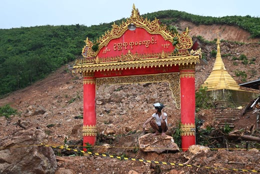A motorcyclist squats on a rock in an area affected by a landslide in Paung township, Mon state on Aug. 10, 2019. The death toll from a landslide triggered by monsoon rains in eastern Myanmar rose to at least 34, an official said on August 10, as emergency workers continued a desperate search through thick mud for scores more feared missing.