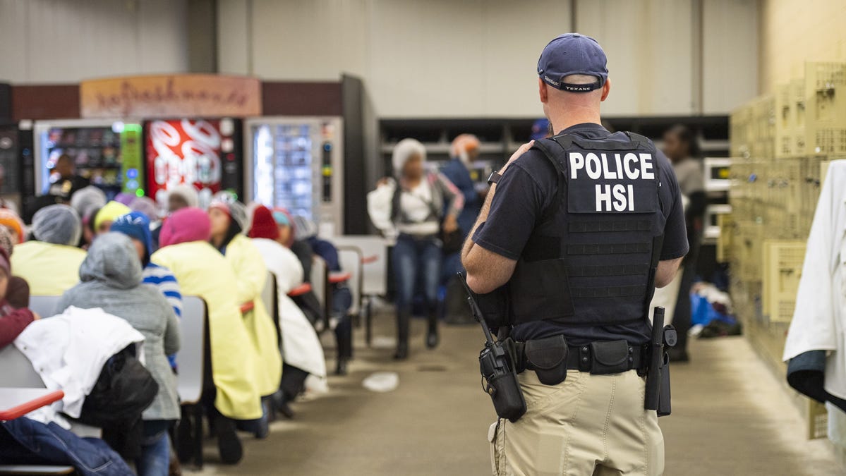 This image released by Immigration and Customs Enforcement (ICE) shows a Homeland Security Investigations (HSI) officer guarding suspected undocumented workers on August 7, 2019.
