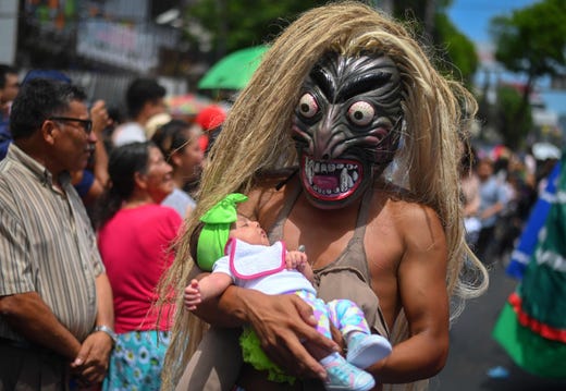 A reveller with a mythological character mask and holding a baby takes part in a parade marking the start of the festival of the Divine Savior of the World, San Salvador's patron saint, in San Salvador, on August 1, 2019.