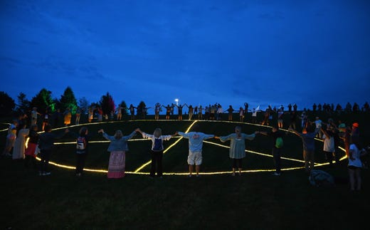 Guests hold hands around a giant illuminated peace sign during the 50th anniversary celebration of Woodstock at Bethel Woods Center for the Arts on Aug. 15, 2019 in Bethel, N.Y. Organizers of the Woodstock weekend, whose 50th anniversary starts Aug. 15, originally wanted to hold the event celebrating peace, love and music in its namesake town, long a haven for creative types including Bob Dylan. For space and permit reasons they were forced to look elsewhere -- about 60 miles southwest -- but opted to retain the Woodstock moniker.