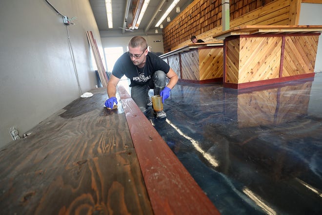 Cody Morgan oils a wooden platform along the wall at Peninsula Beverage Collective in Port Orchard on Thursday.