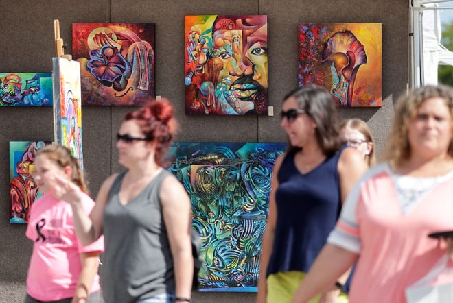 People walk past paintings by artist Gregory Frederic at Artstreet in 2019 in downtown Green Bay. This year's event will move to Ashwaubomay Park in Ashwaubenon.