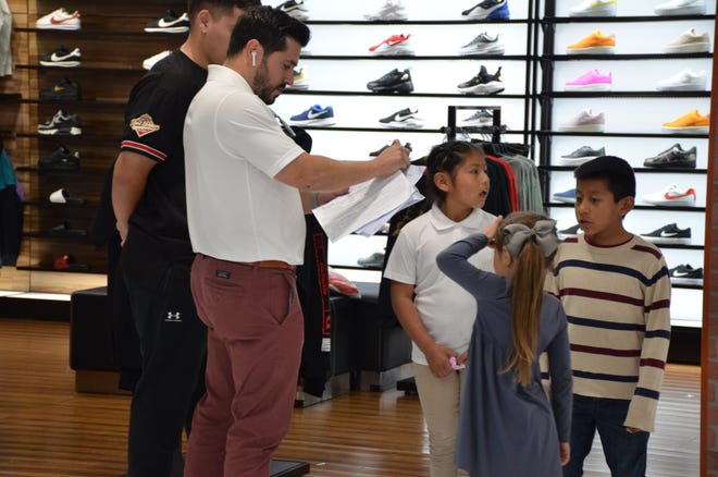 Jorge Edeza, a former student of Sánchez Elementary, helps students Carlos Mendez and Alison Acosta pick shoes at Shoe Pavillion during a back-to-school shopping spree he helped finance with his friends Juan del Real, Miguel Rubio and Sergio Ceja.