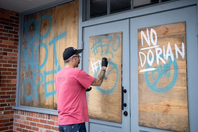 Brian Di Giorgi paints on the plywood over the windows of his grilled cheese and cocktail bar, Crust, in downtown Wilmington, North Carolina as he prepares for Hurricane Dorian on Sept. 4, 2019. The boards are recycled from Hurricane Florence last year which closed the new business for 22 days. "As soon as we can be open again, we're gonna be open again," he said. 