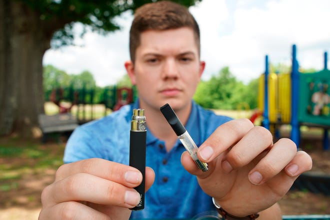 Jay Jenkins holds a Yolo! brand CBD oil vape cartridge alongside a vape pen at a park in Ninety Six, S.C., on Wednesday, May 8, 2019. Jenkins says two hits from the vape put him in a coma and nearly killed him in 2018. Lab testing commissioned by AP showed the vape contained a synthetic marijuana compound blamed for at least 11 deaths in Europe.