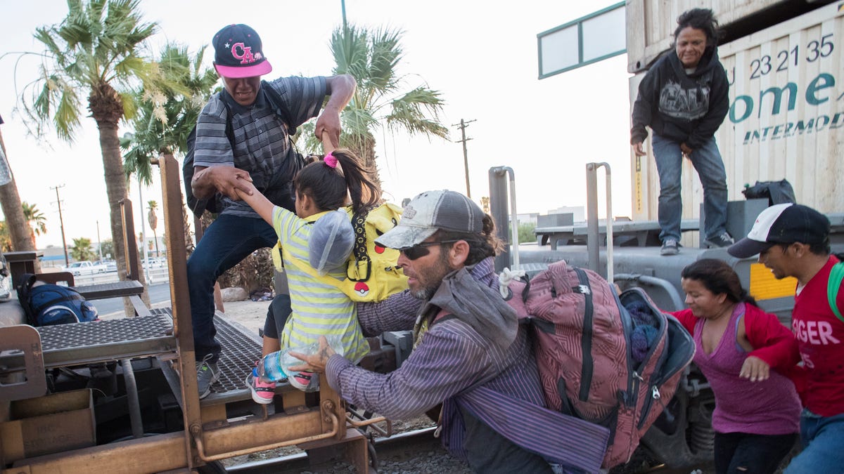 A child boards a moving train with the help of other migrants. The child was helped by adults in the group as her father and mother assisted her two younger siblings. The migrants were headed south after they were returned to Mexico by U.S. officials when they sought asylum.