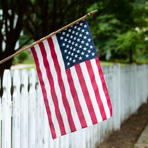 Small American flag hangs from a picket fence alon