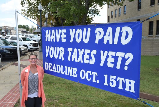 Baxter County Collector Teresa Smith stands next to a large sign on the county courthouse lawn reminding motorists that their property taxes are due later this month.