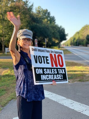 Martha Anderson smiles and waves at passerby on Woodbine Road as she holds a sign opposing the penny tax increase on Tuesday, Oct. 8, 2019.