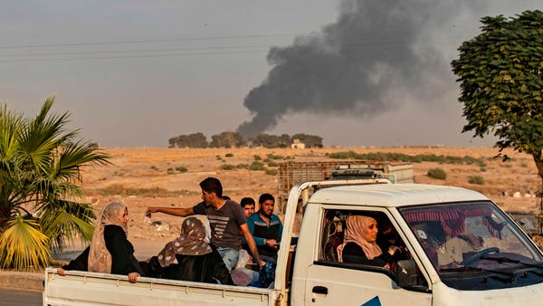 Civilians ride a pickup truck as smoke billows fol