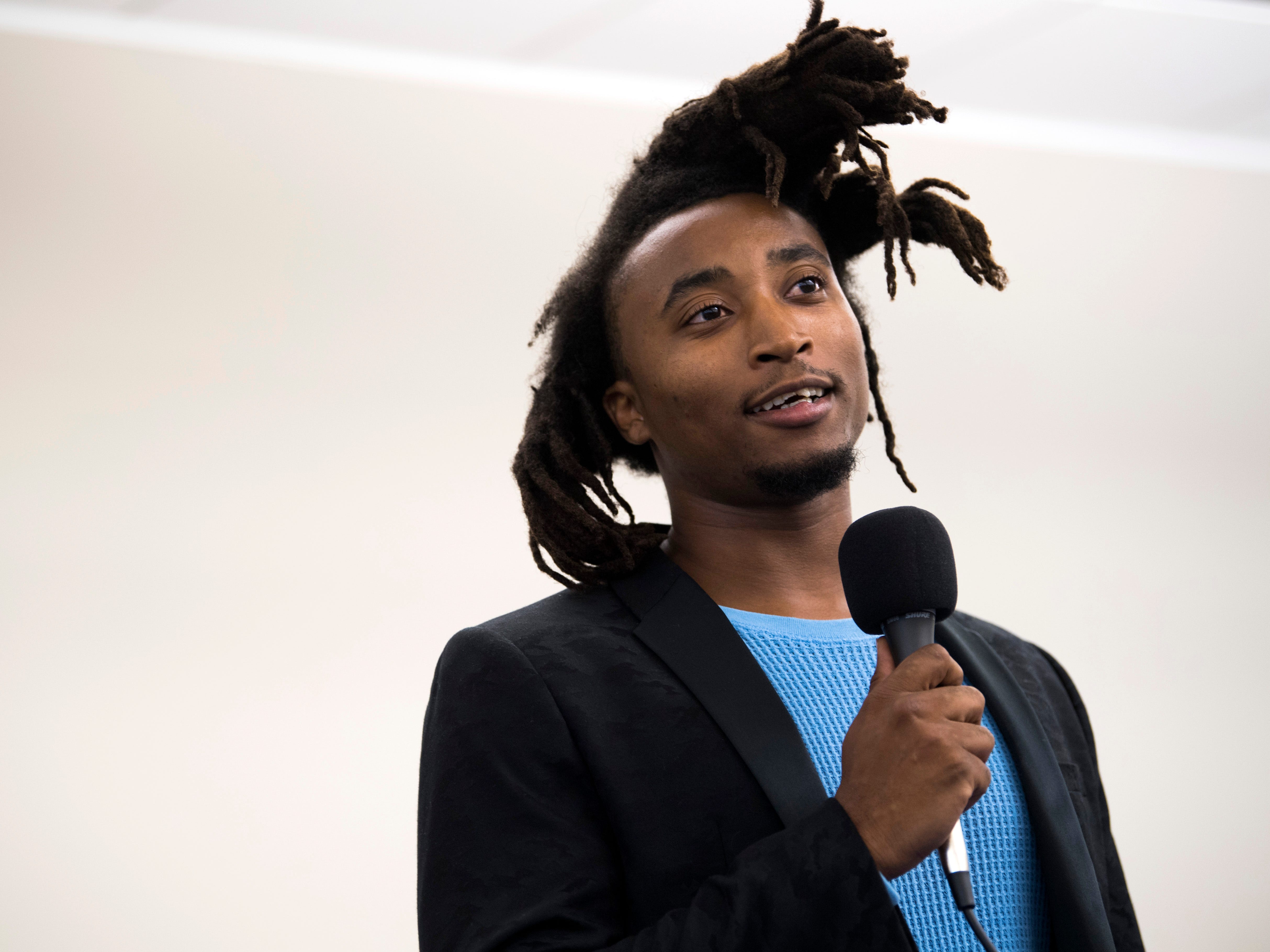 Nzinga Bayano Amani speaks holding a microphone.