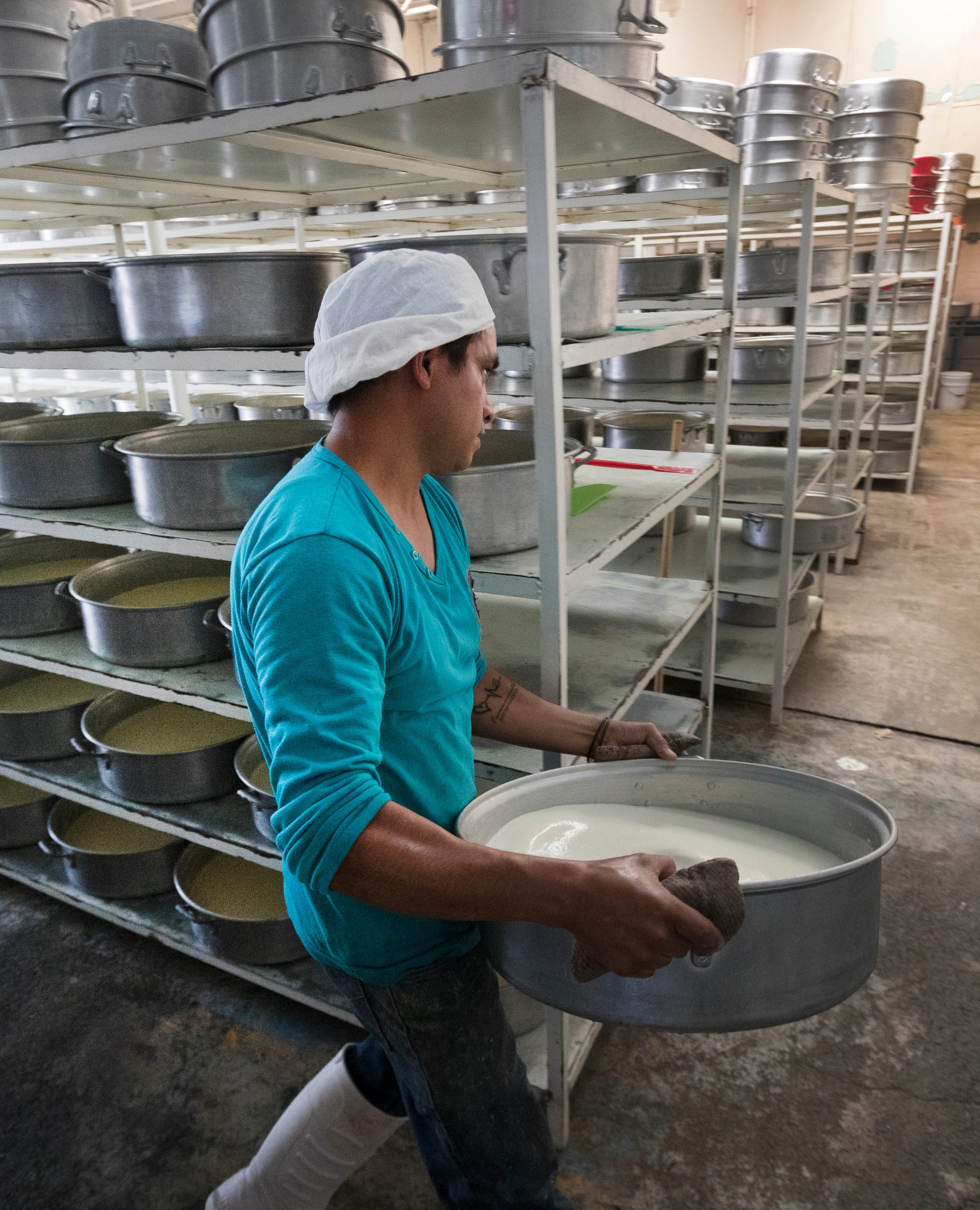 A worker carries a tub of milk that will be processed into cream by evaporation over burners at a small dairy plant owned by Álvaro González and his brother in Tizayuca, Mexico. The business employs 15 people who make cream and yogurt.