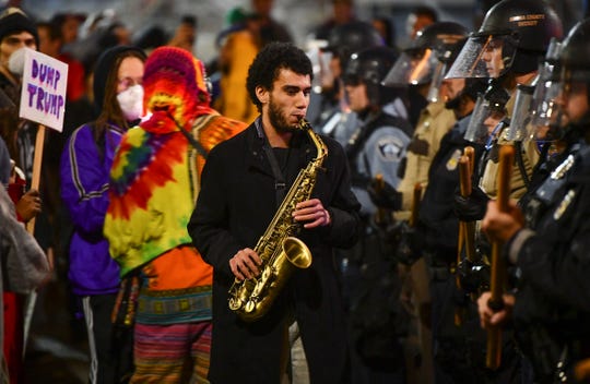 Matthew Trice plays the saxophone between protesters and a police line following the rally for Donald J. Trump Thursday, Oct. 10, 2019, outside the Target Center in Minneapolis. 