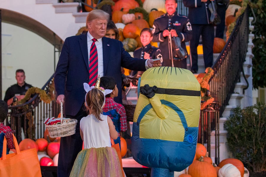 President Donald Trump places a candy bar on the head of child dressed as Minion during a Halloween trick-or-treat event on the South Lawn of the White House which is decorated for Halloween, Monday, Oct. 28, 2019, in Washington.