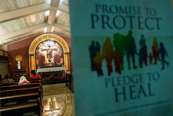 A poster addressing sexual abuse within the Catholic church hangs as parishioners pray at a church in Guam.