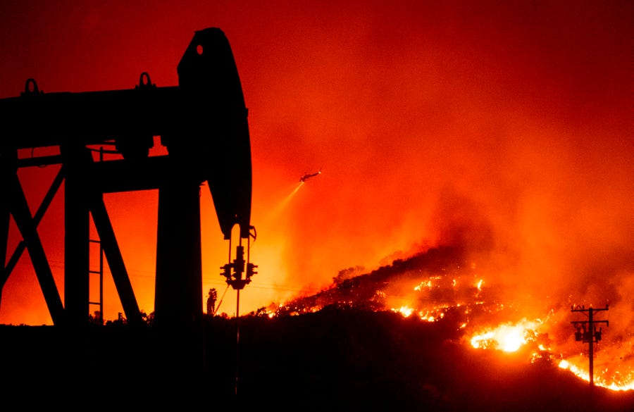 An oil pump jack is silhouetted as a helicopter flies over flames during the Maria Fire in Santa Paula, California, on Nov. 1, 2019. The Maria Fire broke out late October 31 in Ventura County, threatening two small agricultural towns nearby and forcing the evacuation of more than 7,000 people as it raged across 5,000 acres, according to Ventura County fire department. 
