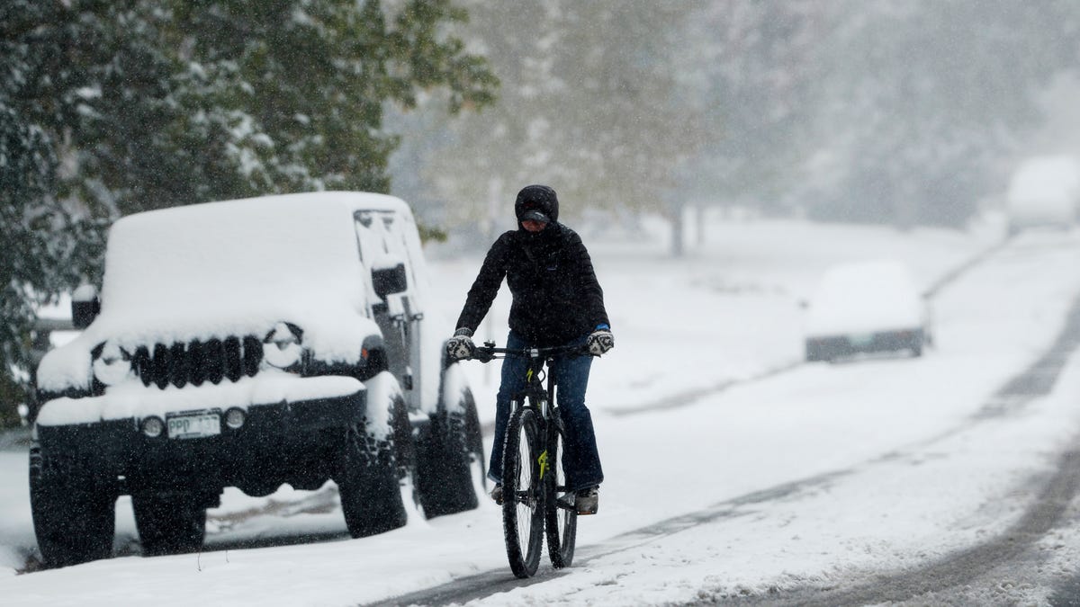 FILE - In this Oct. 10, 2019, file photo, a bicyclist uses a tire track to guide her bicycle down South Monroe Street as the season's first snow storm sweeps over the metropolitan area in Denver. A government agency is recommending that all 50 states enact laws requiring bicyclists to wear helmets to stem an increase in bicycle deaths on U.S. roadways. The recommendation was among several issued by the National Transportation Safety Board after a hearing   Tuesday, Nov. 5, on bicycle safety. (AP Photo/David Zalubowski, File) ORG XMIT: NY203