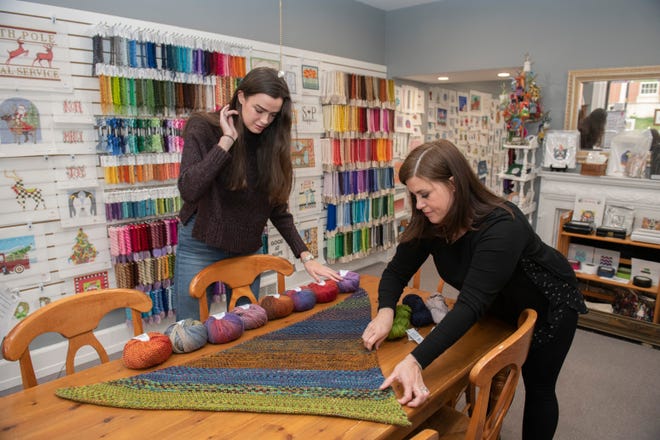 E-commerce and social media intern Kaley MacLeod (left) and yarn manager Elizabeth Wakefield arrange a display of yarn and a hand-knitted shawl called 'Nightshift,' designed by Andrea Mowry (not pictured) and knitted by Wakefield inside The Wool and The Floss knitting shop.