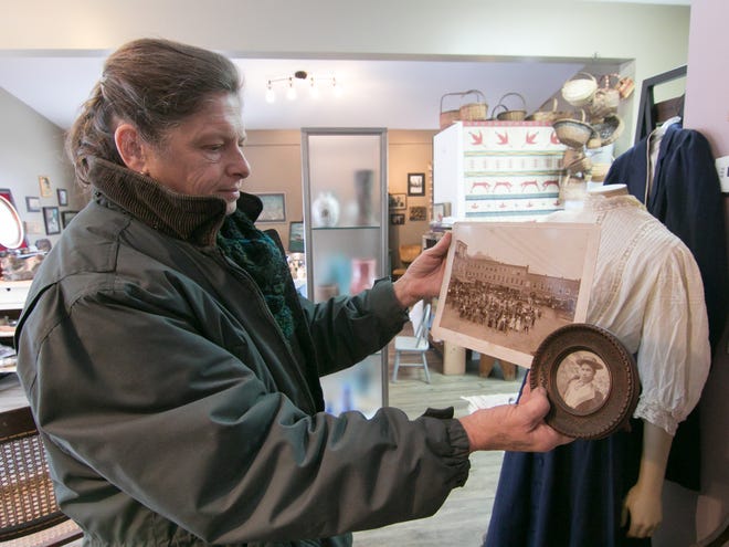 Readying the soon-to-open Rare Findings antique and art store in Genoa Township Wednesday, Nov. 13, 2019, owner Pam Thomas holds a photo of her great grandmother Olive, as well as a group shot of bicyclists including Olive, in front of an outfit Olive wore in the group photo of bicyclists in Woodstock, Vermont in 1916.