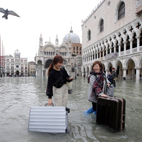 Tourists push their luggage in a flooded St. Mark'