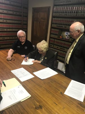 St. Landry Parish president Bill Fontenot and Opelousas attorney Patrick Morrow watch as Mavis Fontenot representing the St. Luc French immersion non-profit group signs a bill of sale allowing the purchase of a former community hospital in Arnaudville from St. Landry Parish government.