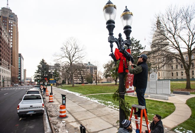 Jon Babcock, top, Brandon Cook, and John Miller, right, of All Star Media  in Lansing mount jobo lights Tuesday, Nov. 19, 2019, that will project snowflakes and the Silver Bells in the City logo onto City Hall this Friday evening, during the 35th annual Silver Bells in the City event.