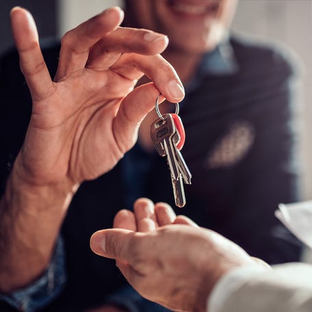 Real estate agent sitting at the desk by the window and passing keys to his client in the office